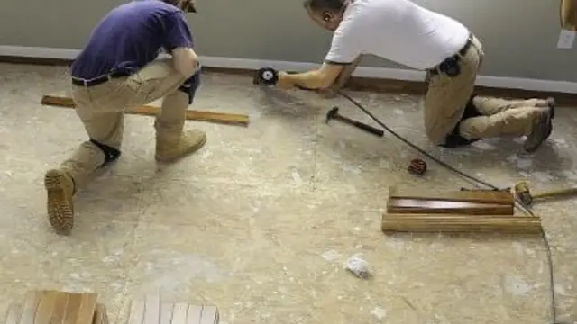 Two workers kneeling on a bare subfloor with hand tools during a flooring repair
